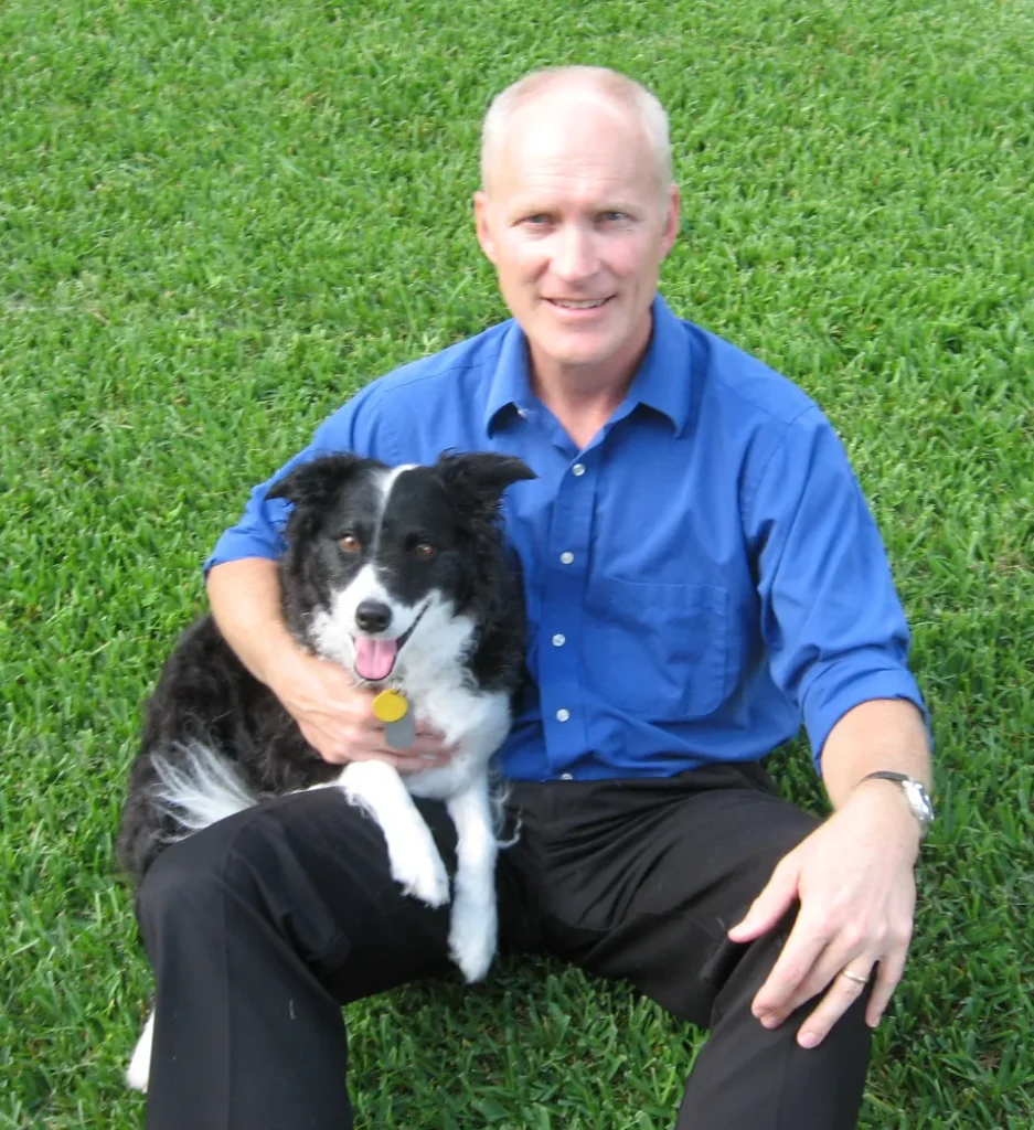 Dr. Mike Elliott sitting on the grass with a black-and-white dog